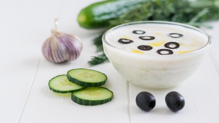 Freshly made tzatziki in a glass bowl with olives on a white wooden table. Vegetarian Greek cuisine.の写真素材