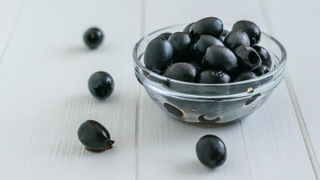 Cup with scattered olives on a white table. Fresh olives in a glass bowl.の写真素材