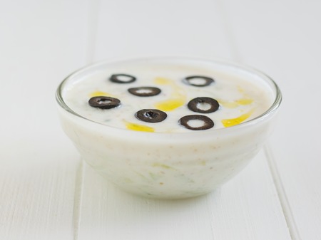 Tzatziki sauce bowl decorated with olives on a white wooden table. Vegetarian Greek cuisine.の写真素材