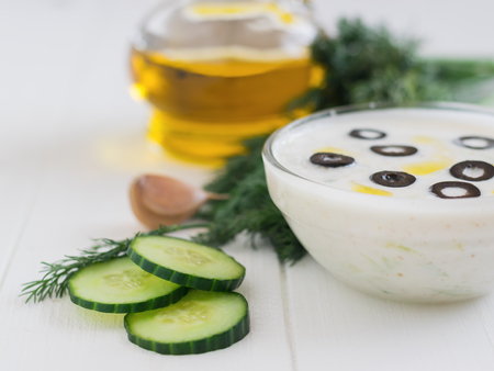 Freshly made tzatziki in a glass bowl with olives on a white wooden table. Vegetarian Greek cuisine.の写真素材