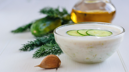 Freshly made tzatziki in a glass bowl with olives on a white wooden table. Vegetarian Greek cuisine.の写真素材