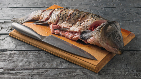 Cut into pieces carp fish with a knife on a cutting Board. Cooking dinner of river fish.の写真素材
