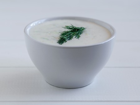 White bowl with tzatziki and a sprig of dill on white wooden table.の写真素材