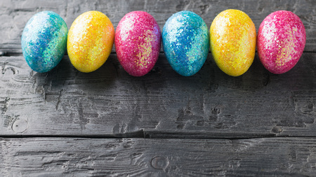 Multicolored Easter eggs are laid in a horizontal line on a wooden table. The decoration of the Easter table.の写真素材