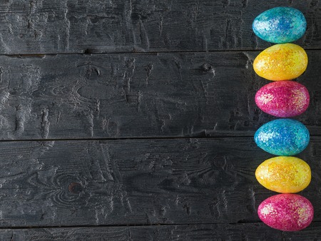 Multicolored Easter eggs are laid in a vertical line on a wooden table. The decoration of the Easter table. Great Christian holiday.の写真素材
