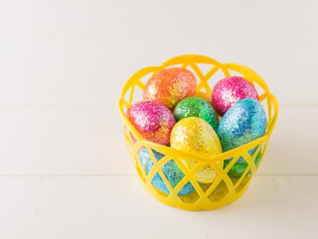 Yellow basket with colorful eggs on a white rustic table. Decorations for the Easter table.の写真素材