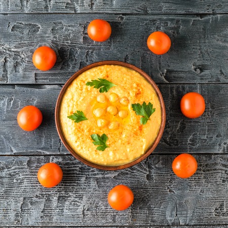 Bowl with fresh hummus and eight cherry tomatoes on a wooden table. Vegetarian middle Eastern dish and chickpea.の写真素材