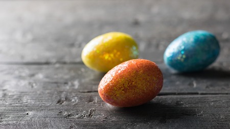 Three colorful eggs on a dark wooden table. The decoration of the Easter table. Great Christian holiday.の写真素材