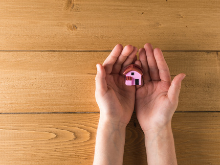 Model house in the hands of a child on a wooden table. The view from the top.の写真素材