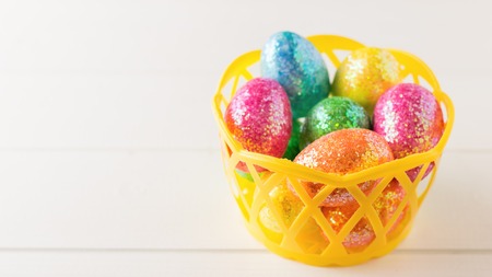 Yellow basket with colorful eggs on a white rustic table. Decorations for the Easter table.の写真素材