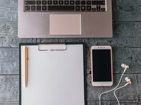 Laptop, tablet with paper, smartphone, pen and earphones on wooden table. The view from the top.の写真素材