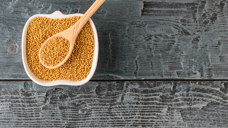 Spoon and Cup with mustard seeds on a dark wooden table. Mustard seed sauce. The view from the top.