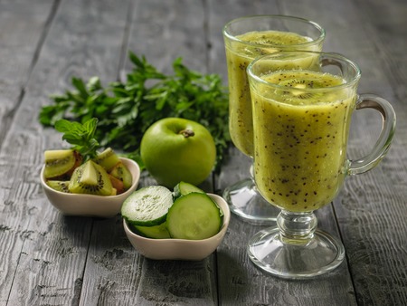 Freshly prepared smoothie of kiwi, Apple, parsley and cucumber and kiwi slices on the rustic table. Healthy and nutritious vegetarian drink of fresh fruits and vegetables.の写真素材