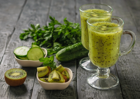 Two glasses of freshly made kiwi and cucumber smoothies on a black wooden table.の写真素材