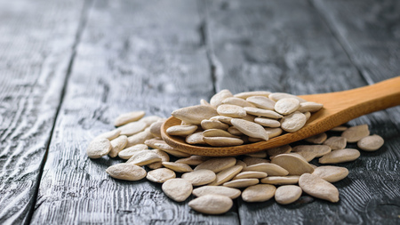A bunch of pumpkin seeds and spoon on a dark rustic table. Vegetarian cuisine.