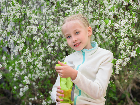 Girl in sports clothes holding a bottle of refreshing drink in cherry blossoms. Portrait of a girl on a background of cherry blossoms.の写真素材