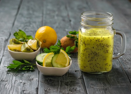 Mug with smoothies of kiwi, cucumber, lemon, parsley and mint on a rustic black table.の写真素材