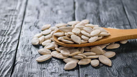 A spoon with pumpkin seeds on a dark rustic table.の写真素材