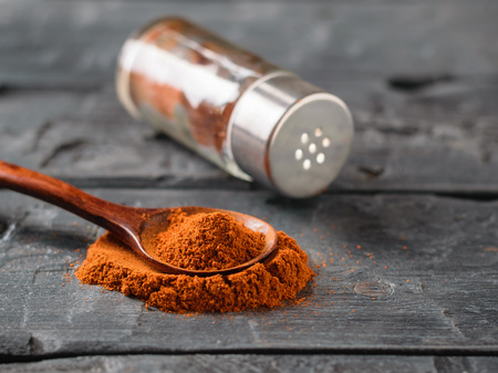 A pepper jar and a spoon of ground chili on a rustic table.の写真素材