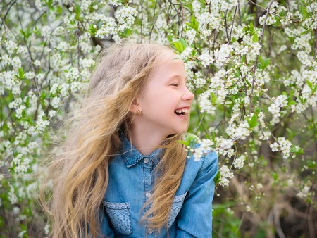 Portrait of a girl at cherry. Girl with her hair down in a denim shirt in a cherry blossom garden. Portrait of laughing happy girl.の写真素材