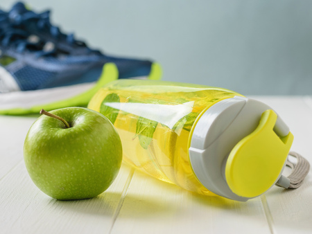 Sports bottle with a refreshing drink and a green Apple on the background of running shoes.の写真素材