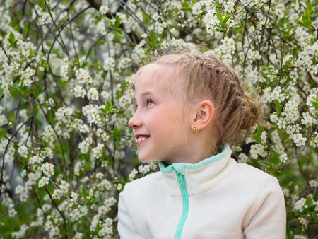 Beautiful girl in sports jacket fun looking in the direction in cherry Park. Portrait of a girl on a background of cherry blossoms.の写真素材