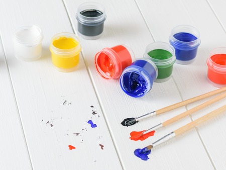 Scattered on a wooden table jars of gouache and three multi-colored brushes. Creative kit. Hobby and style.の写真素材