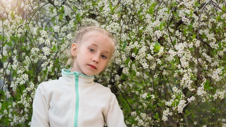 Beautiful girl in sports clothes in a blooming Park at sunset. Portrait of a girl on a background of cherry blossoms.の写真素材