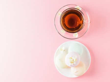 A Cup of tea and a bowl of colored marshmallows on a pink table. The view from the top.Spring tea composition on a white table. Flat lay.の写真素材