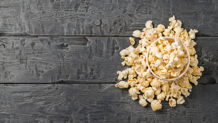 Popcorn is poured from a multi-colored paper Cup on a rustic table. Vegetarian food from corn.の写真素材
