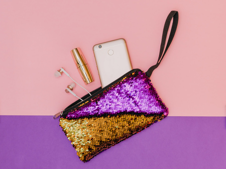 Purple with gold women's handbag with phone lipstick and bracelet on a two-color table. Pastel color. Women's accessories. Flat lay.の写真素材
