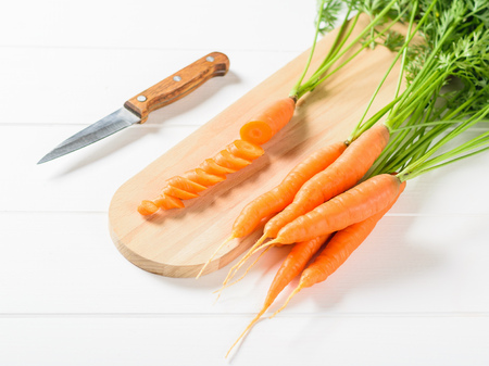 A bunch of fresh carrots and sliced carrots with a knife on a white wooden table. The concept of vegetarian food with natural raw products.の写真素材