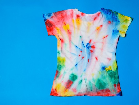 T-shirt painted in tie dye style on a blue background. White clothes painted by hand. The view from the top. Flat lay.の写真素材