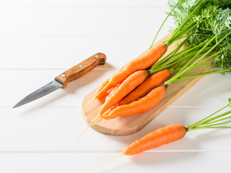 Sliced carrots with a knife on a cutting Board and a bunch of carrots on a white table. The concept of vegetarian food with natural raw products.の写真素材