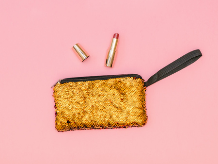 Golden women's handbag with lipstick on a pink table. Pastel color. Women's accessories. Flat lay.の写真素材