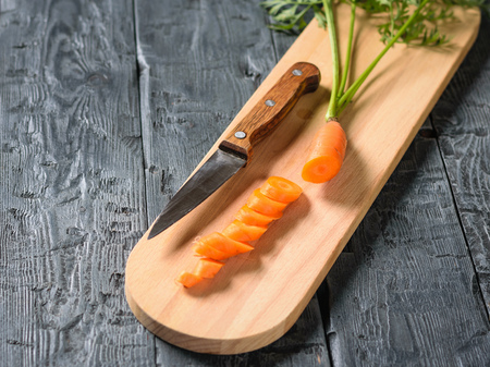 Sliced carrots with a knife on the cutting Board on the village table. The concept of vegetarian food with natural raw products.の写真素材