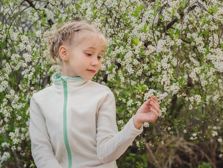 Beautiful girl in sports clothes in a blooming Park at sunset. Portrait of a girl on a background of cherry blossoms.の写真素材