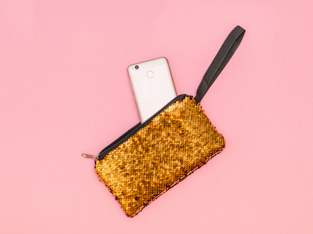 Women's handbag with a sticking phone of gold color on a pink table. Pastel color. Women's accessories. Flat lay.の写真素材
