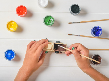 Girl with colored nails paints the body of a wooden truck. Creative kit. Hobby and style.の写真素材
