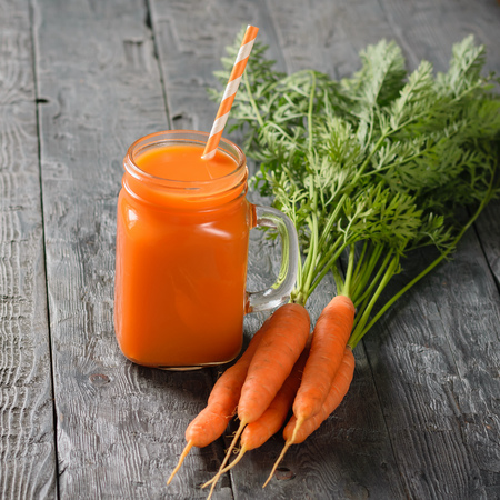A mug of fresh carrot smoothie with cocktail straw and carrots on a dark wooden table. The concept of healthy eating.の写真素材