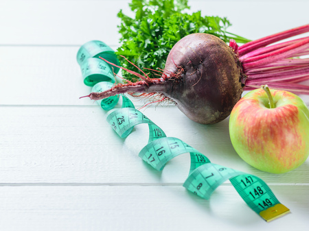 Apple, beetroot, parsley beam and measuring tape on white wooden table. The concept of dietary food...