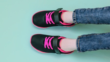 Girl's legs in ripped jeans and black and red sneakers on blue pastel background. Fashionable sports...