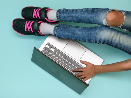 Girls legs in beautiful shoes in front of an open laptop at blue background. Modern education. The...