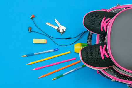Backpack with sneakers and scattered school accessories and house keys on a blue table. Child's school accessories. The view from the top. Flat lay.の写真素材