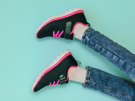 Girl's legs in ripped jeans and black and red sneakers on blue pastel background. Fashionable sports...
