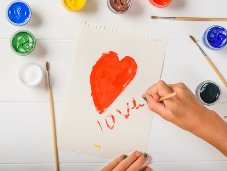The girl paints a heart with red paint and writes the word love. Creative kit. Hobby and style. Flat lay.の写真素材