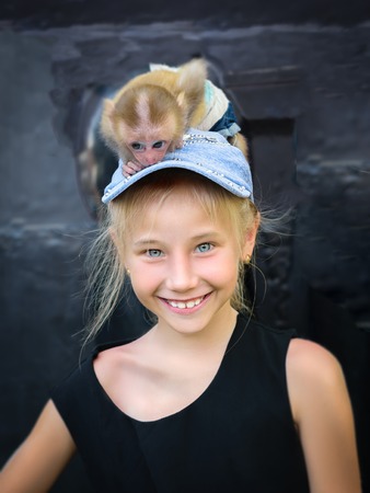 Cheerful girl in a denim cap with a monkey on her head. Communication between humans and animals.