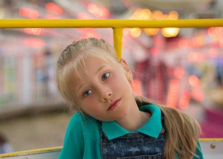 Beautiful sad girl on the background of amusement Park lights. Portrait of a sad child near the Park with attractions.の写真素材
