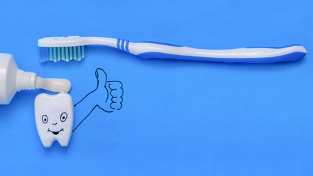 Tooth figurine with funny face and hand shows the class of toothpaste and brush. Oral care products. The view from the top. Flat lay.の写真素材