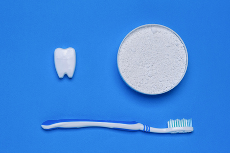 A jar of tooth cleaning powder, a blue toothbrush and a tooth figurine on a blue table. Oral care products. The view from the top. Flat lay.の写真素材